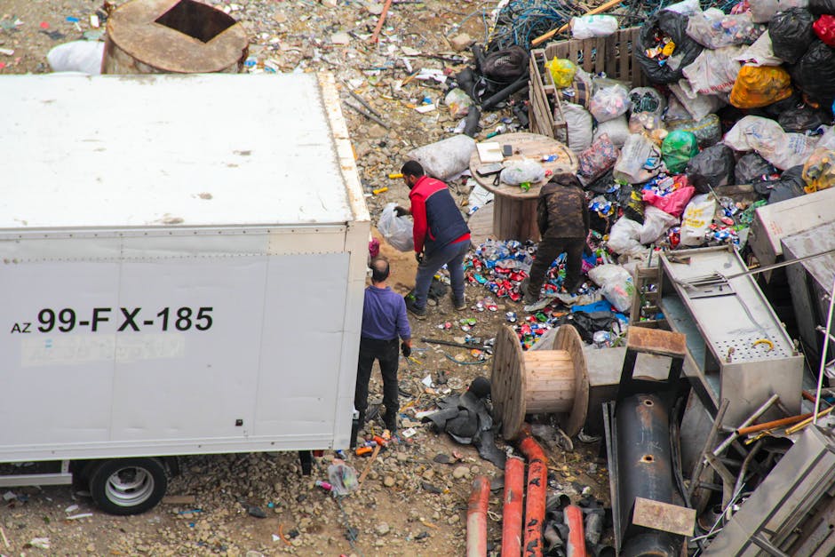 A group of four white household appliances, including washing machines and a tumble dryer, all with circular glass doors, are stacked and arranged on a concrete floor against a plain, unfinished concr